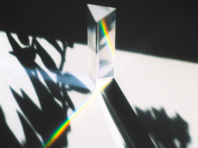 Um prisma de vidro refrata a luz sobre uma superfície, entre sombras de folhas.